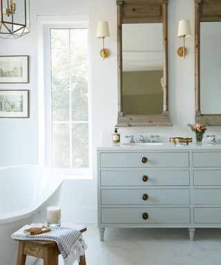 Elegant white bathroom with antique mirrors, brass wall lights and a light blue vanity unit