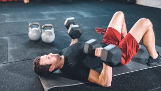 Man performs floor press with dumbbells