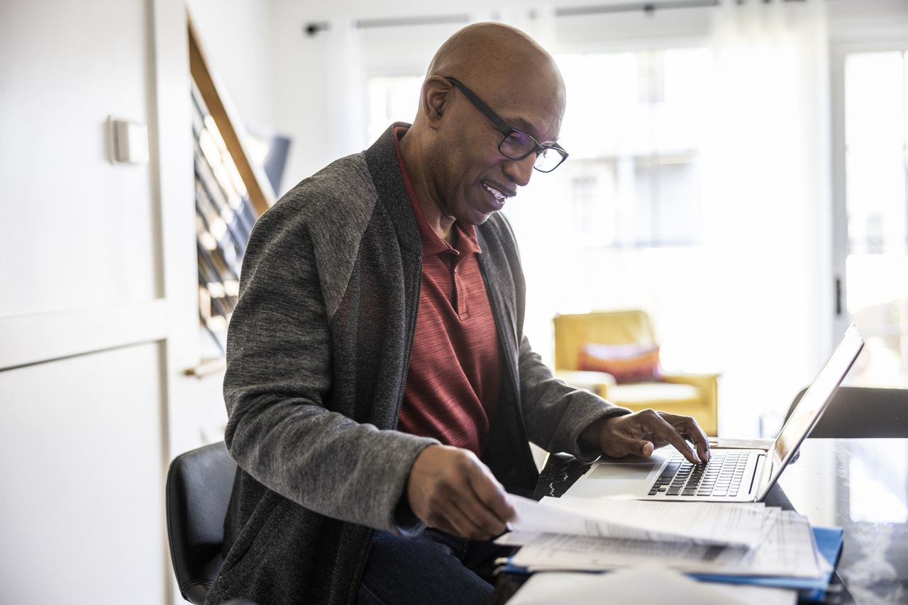 Man looks at financial statements as he sits at desk beside laptop.