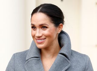 Meghan Markle in a coat smiling at the camera