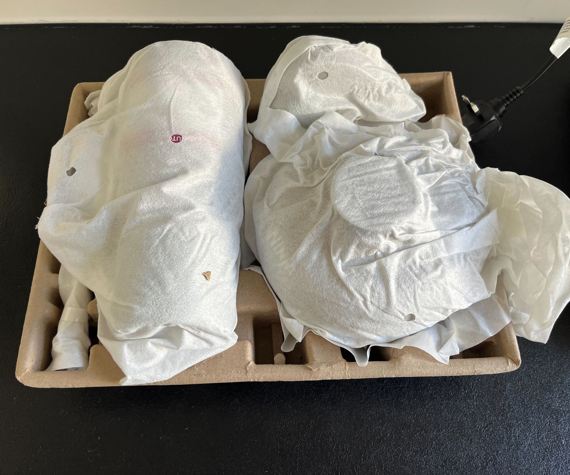 A brown cardboard tray with white fabric wrapped parts inside. 