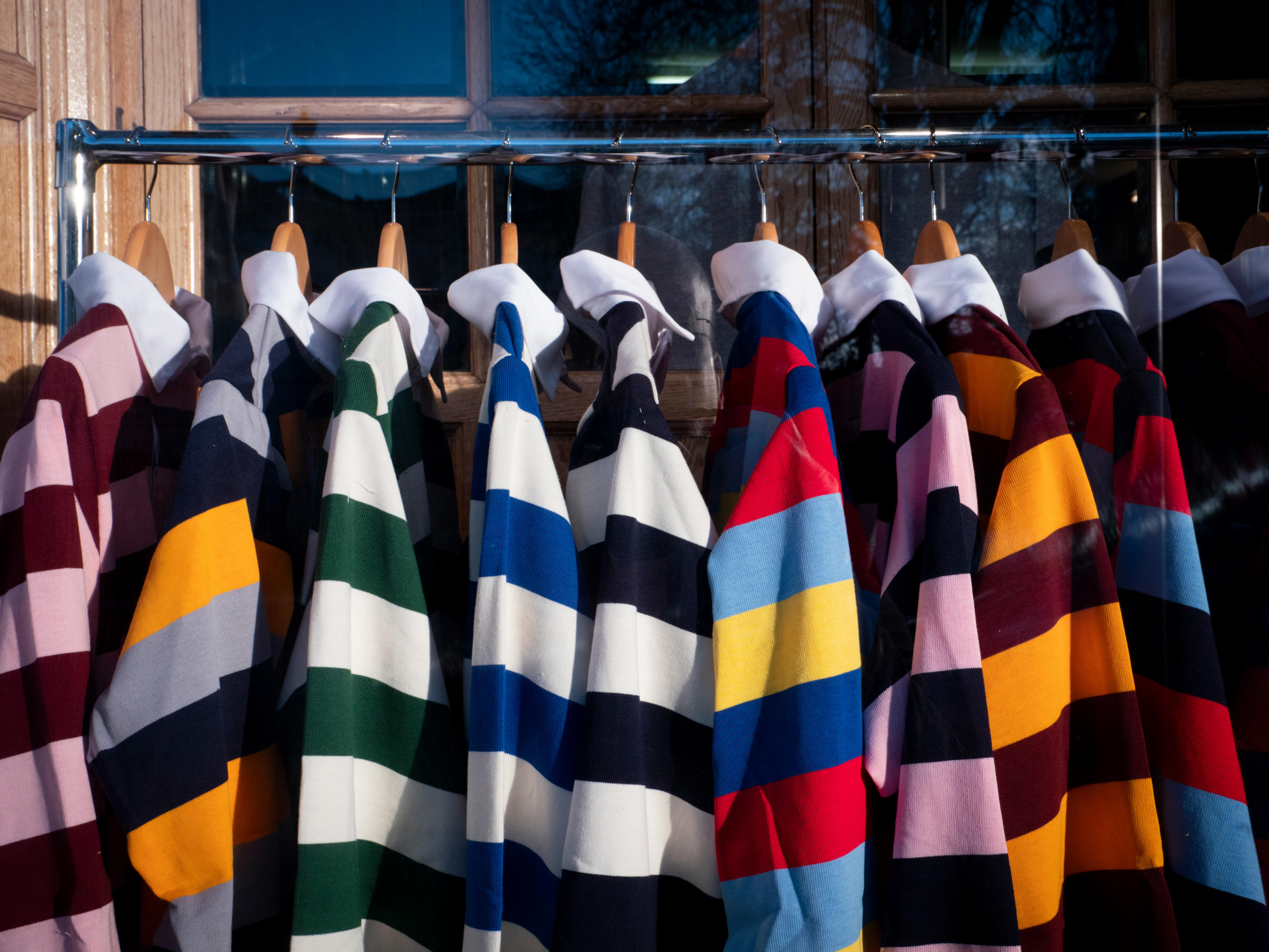 Colourful Cambridge University college rugby shirts hanging up for sale in a shop window display in Cambridge UK