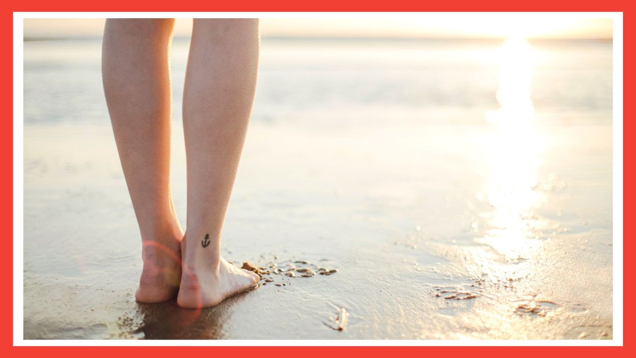 image of the back of woman&#039;s legs with a small ankle tattoo ideas, looking out to the sea on the beach with a red border around the image