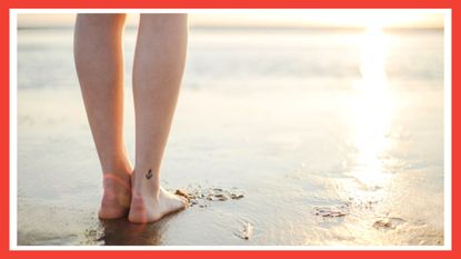 image of the back of woman's legs with a small ankle tattoo ideas, looking out to the sea on the beach with a red border around the image