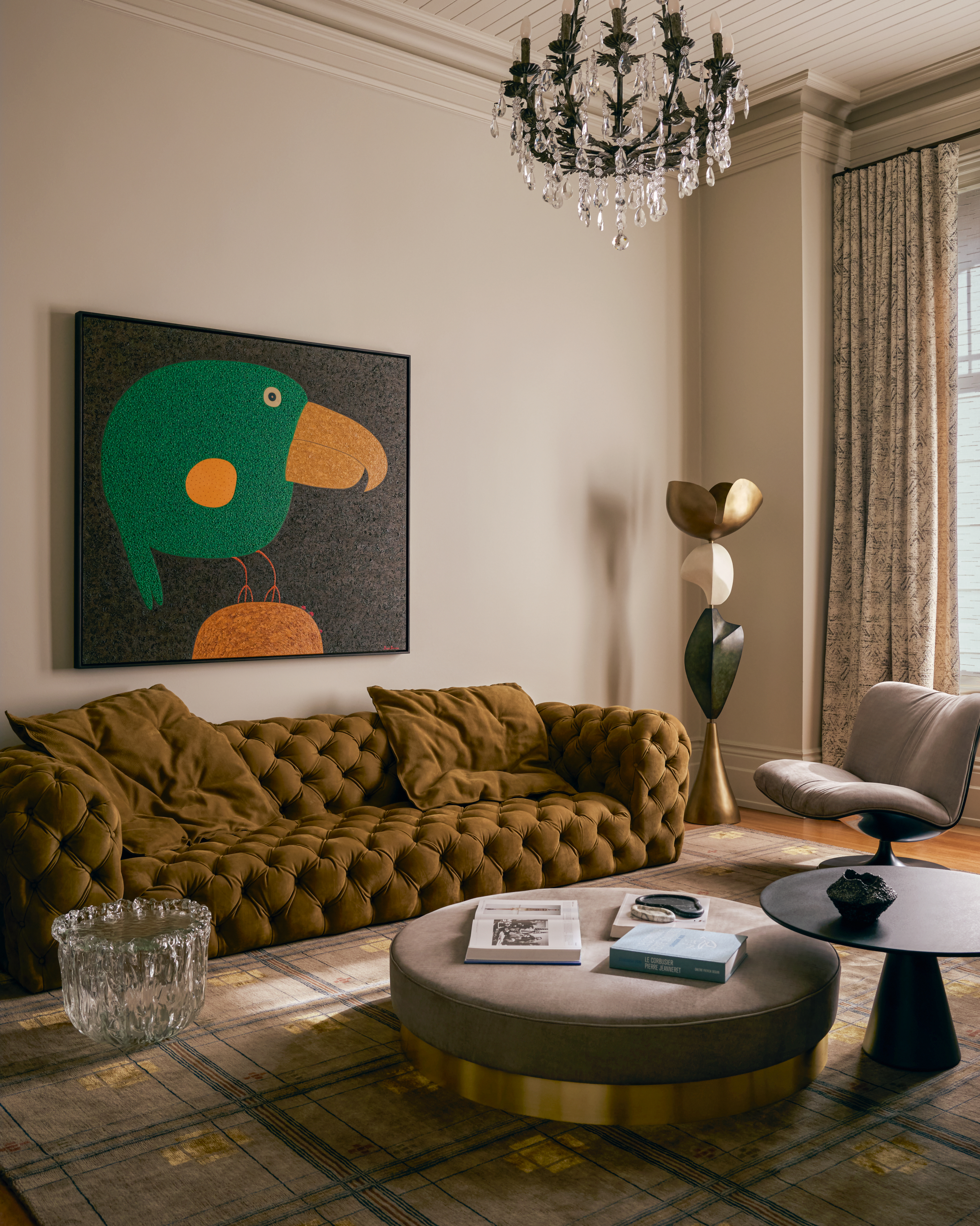 Living room with light beige walls, khaki sofa, toucan artwork, taupe velvet ottoman and ceramic totem-style sculpture