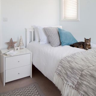 Small white single bedroom, with a cot bed positioned with one side against the wall