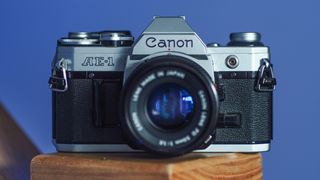 Canon AE-1 film camera on a wooden surface in front of a purple background