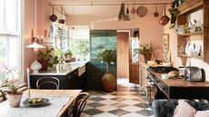 Open plan pink kitchen with dark cabinets and a table and sofa area