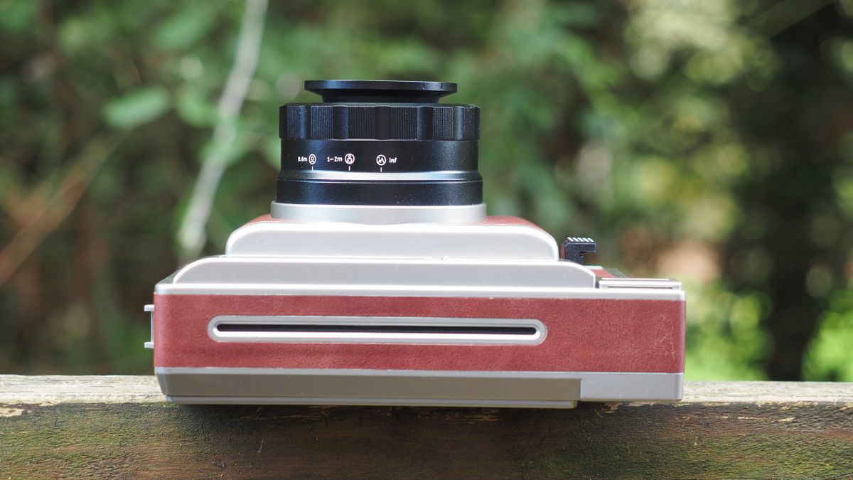 Lomo'Instant Wide Glass camera, sitting on a wooden surface, outdoors against a woodland background