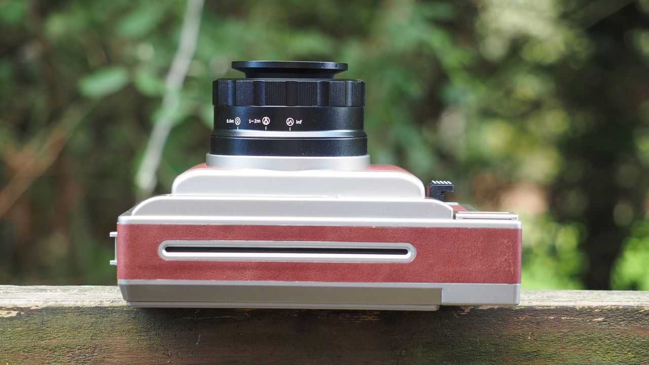 Lomo'Instant Wide Glass camera, sitting on a wooden surface, outdoors against a woodland background