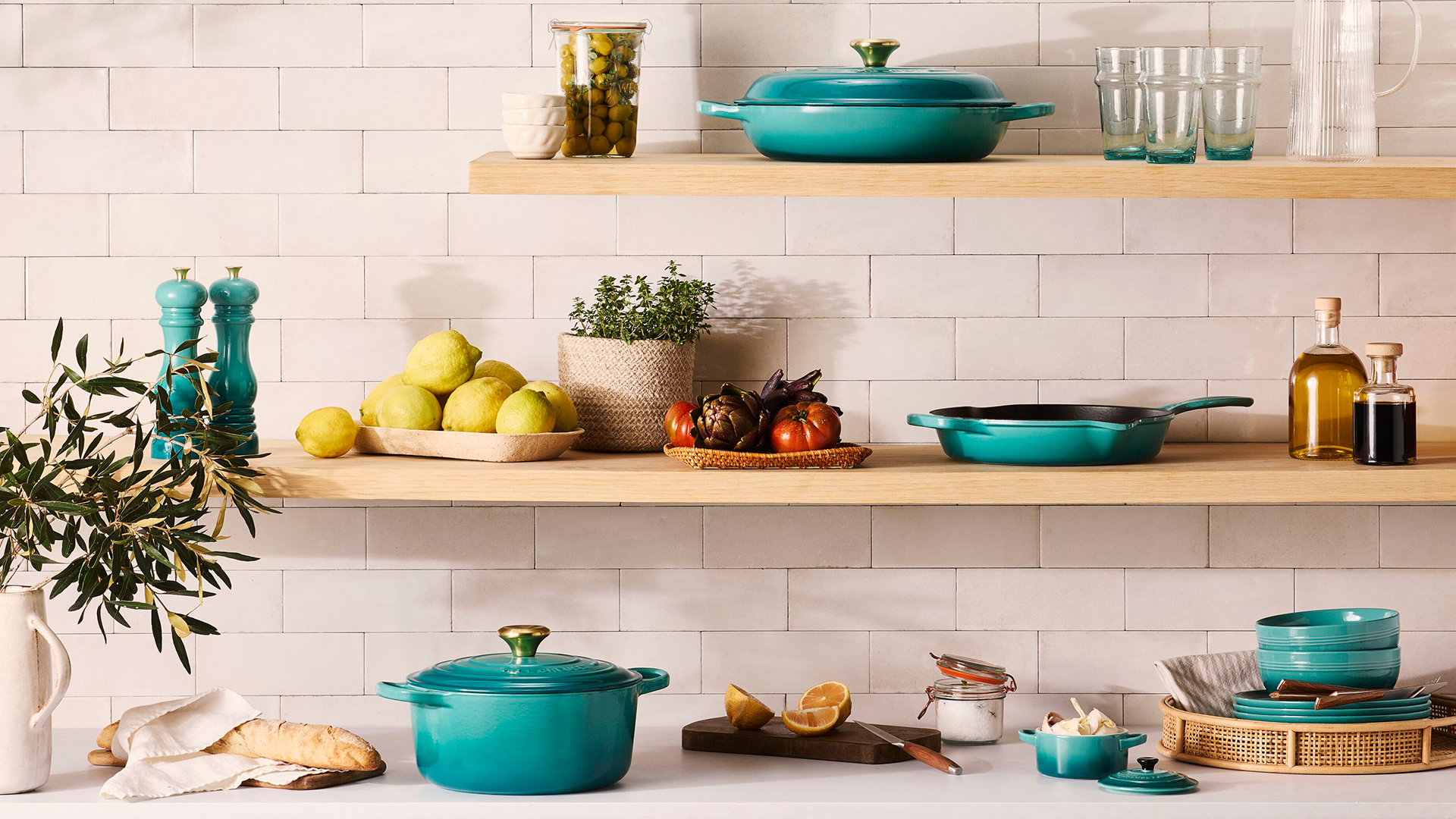 White tiled kitchen with wooden shelves showcasing the Le Creuset Bleu Riviera cast iron cookware