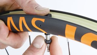 This image is a close up of someone inserting a valve core in to a rim ready to run tubeless tyres.