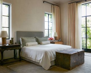 neutral bedroom with gray bed, wooden trunk and metal framed windows