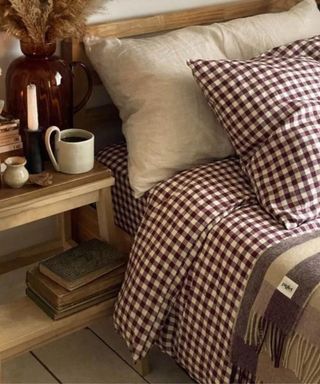 Berry gingham bedding on a bed next to a nightstand piled with dandles and books
