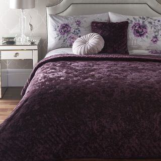 bedroom with white designed wall white drawer brown flooring and bed with purple blanket and floral pillow