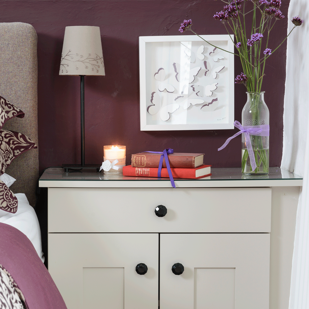 Purple wall with white side table with a vase
