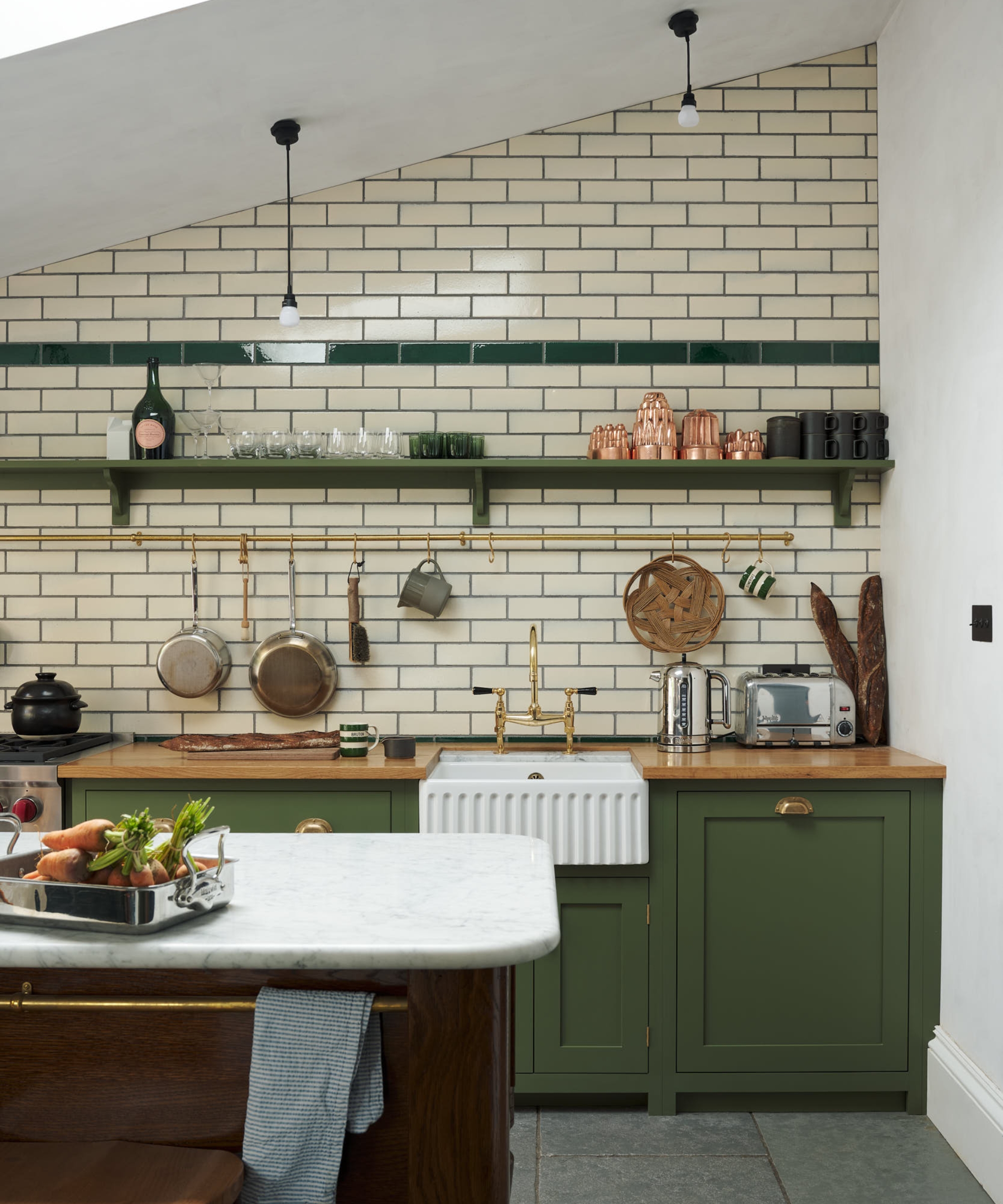 A entire kitchen wall is tiled in cream and green tiles to complement a green kitchen