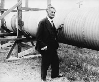 Dr. Albert A. Michelson stands next to a large tube supported by wooden beams.
