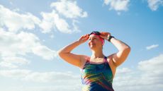 Woman smiling, putting goggles on her head, wearing swimming costume in the sunshine