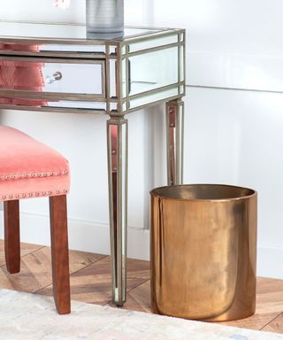 A copper trash can next to a silver vanity and pink chair