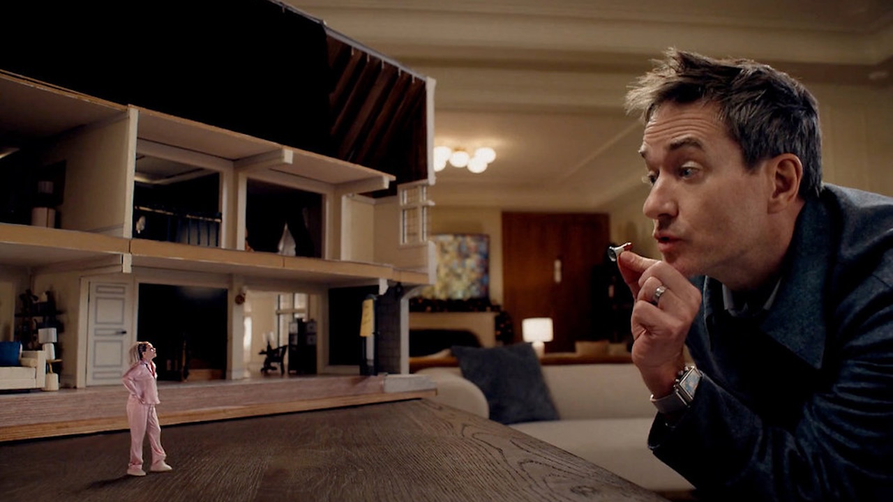 Elizabeth Banks tiny in front of a dollhouse, while Matthew Macfadyen talks to her in The Miniature Wife