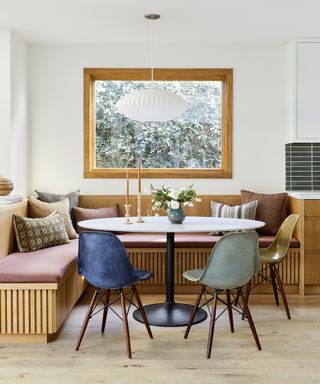 A dining nook with built-in white oak bench, white quartz table and multi-colored Eames-style chairs