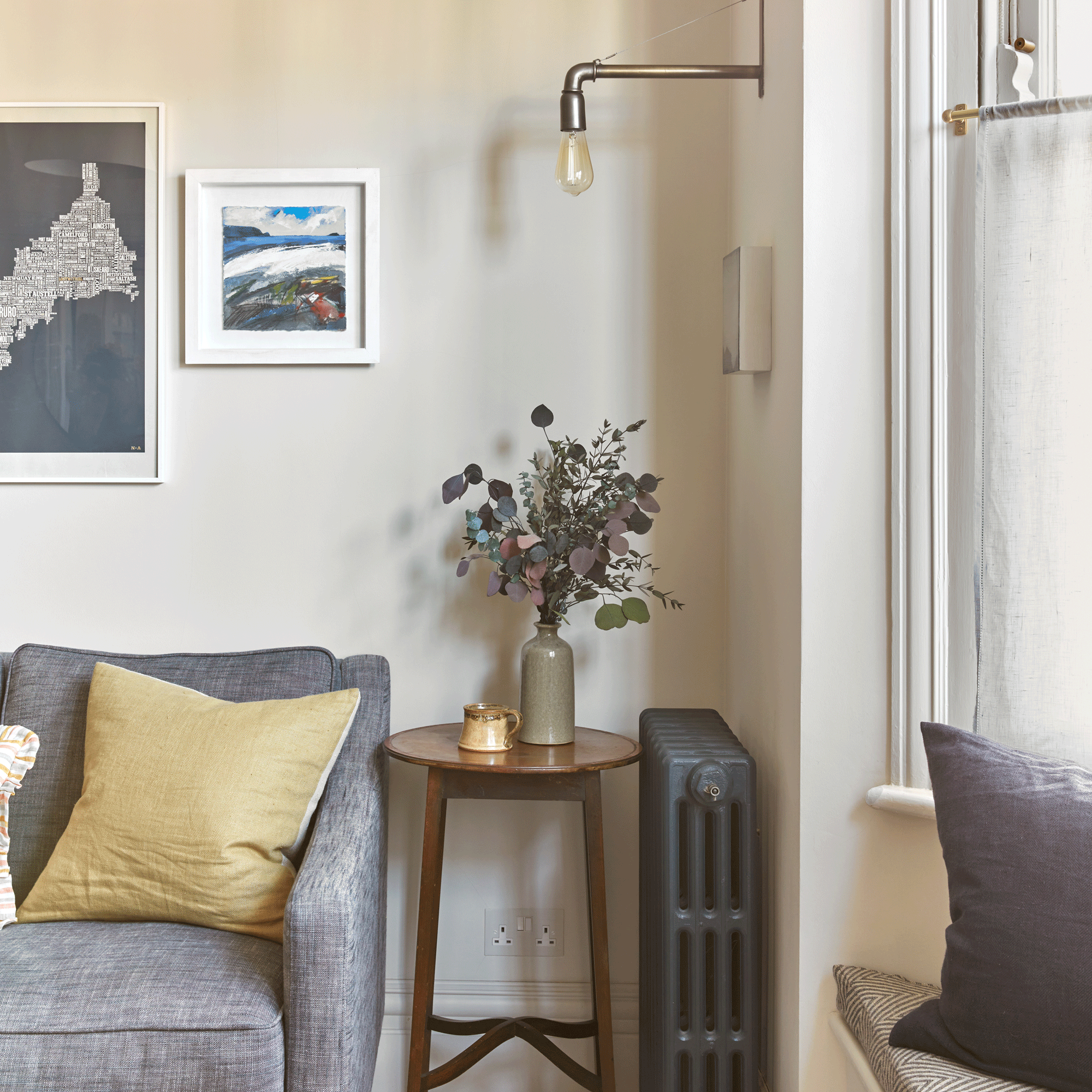 a living room with sash windows and a traditional radiator beside a sofa, side table and wall light