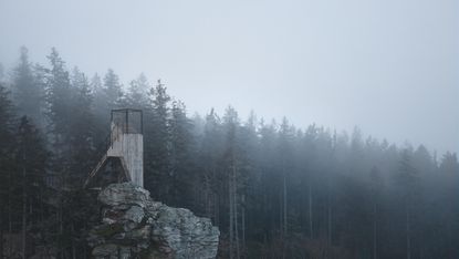 The Miner by Mjölk Architects is a mountain viewpoint, seen here on rocky outcrop, with backdrop of trees, in low cloud