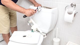 Person in shorts with large adjustable spanner fixing a toilet