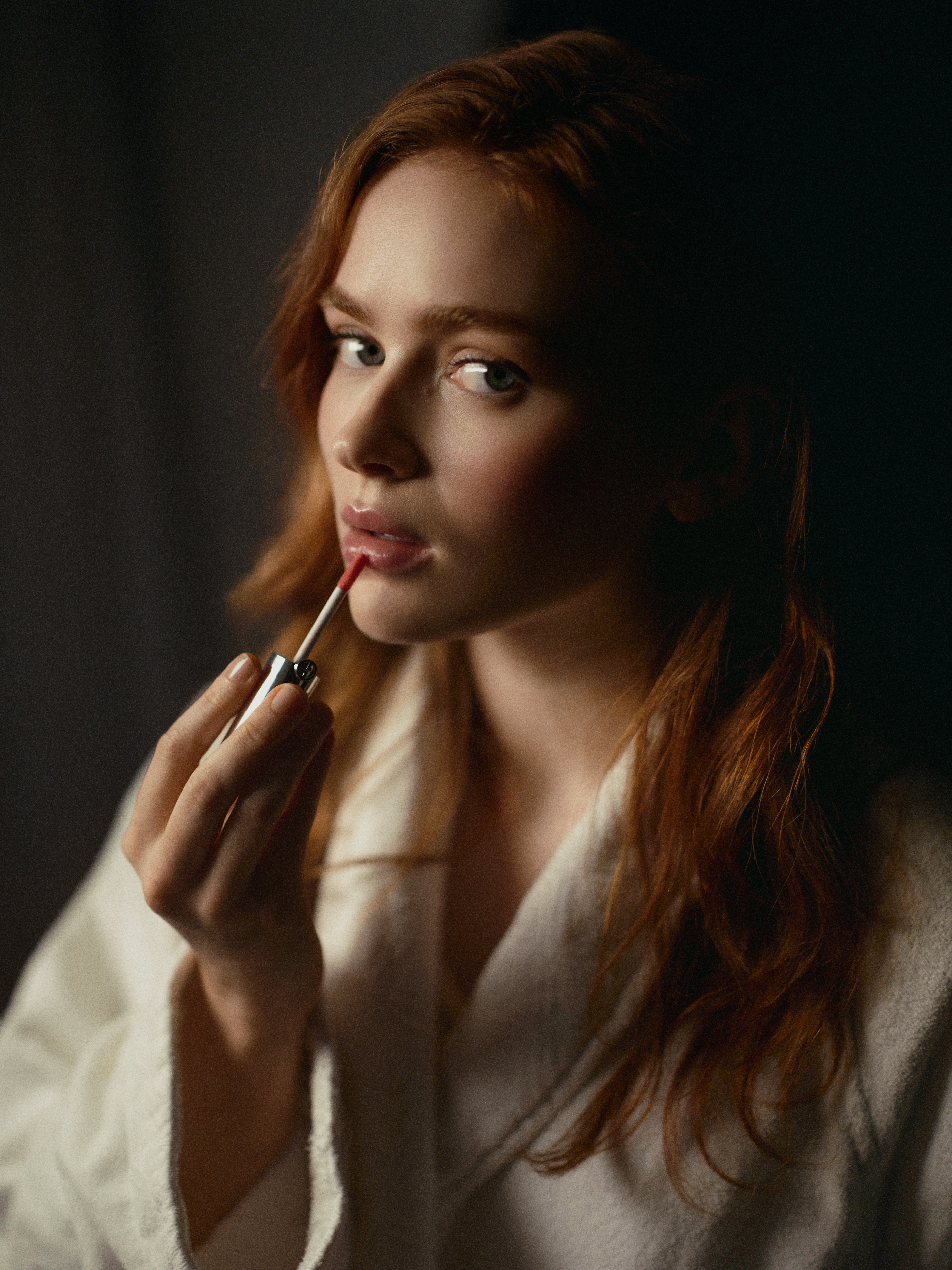 Sadie Sink putting on lipgloss in a robe