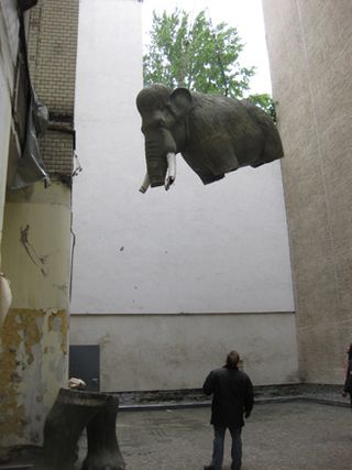 Legless elephant sculpture hanging from building