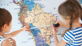 little boy and girl measure distance on world map using measuring tape