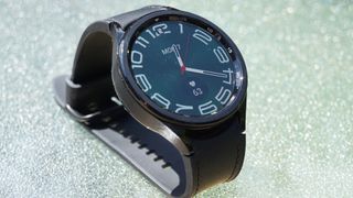 En svart Samsung Galaxy Watch 6 Classic 47mm ligger på ett ljust bord.