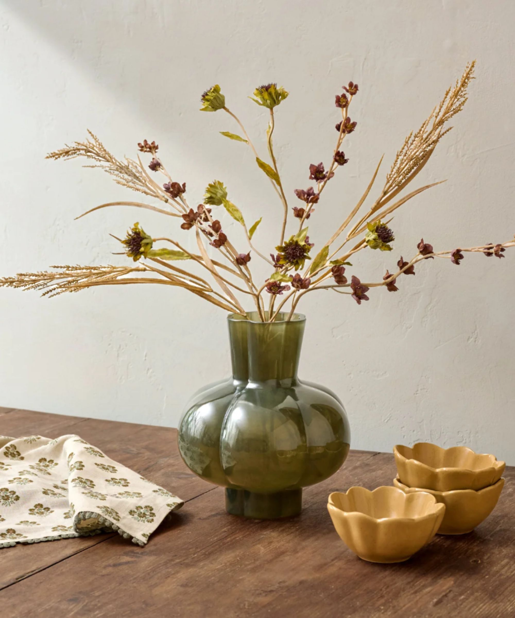 Autumn floral bouquet in scalloped green glass vase next to yellow scalloped pinch bowls