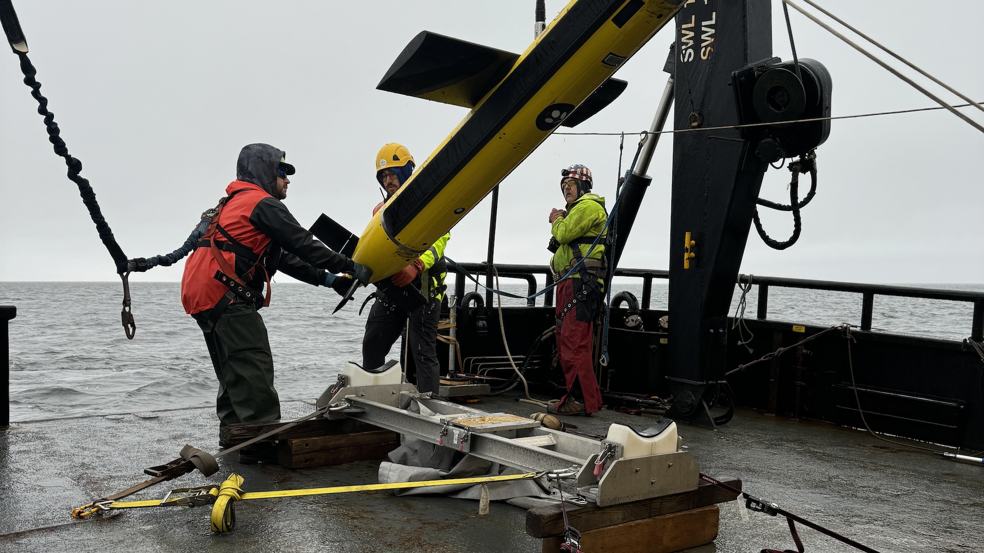 Pesquisadores operam uma grande estrutura amarela que está suspensa em um navio