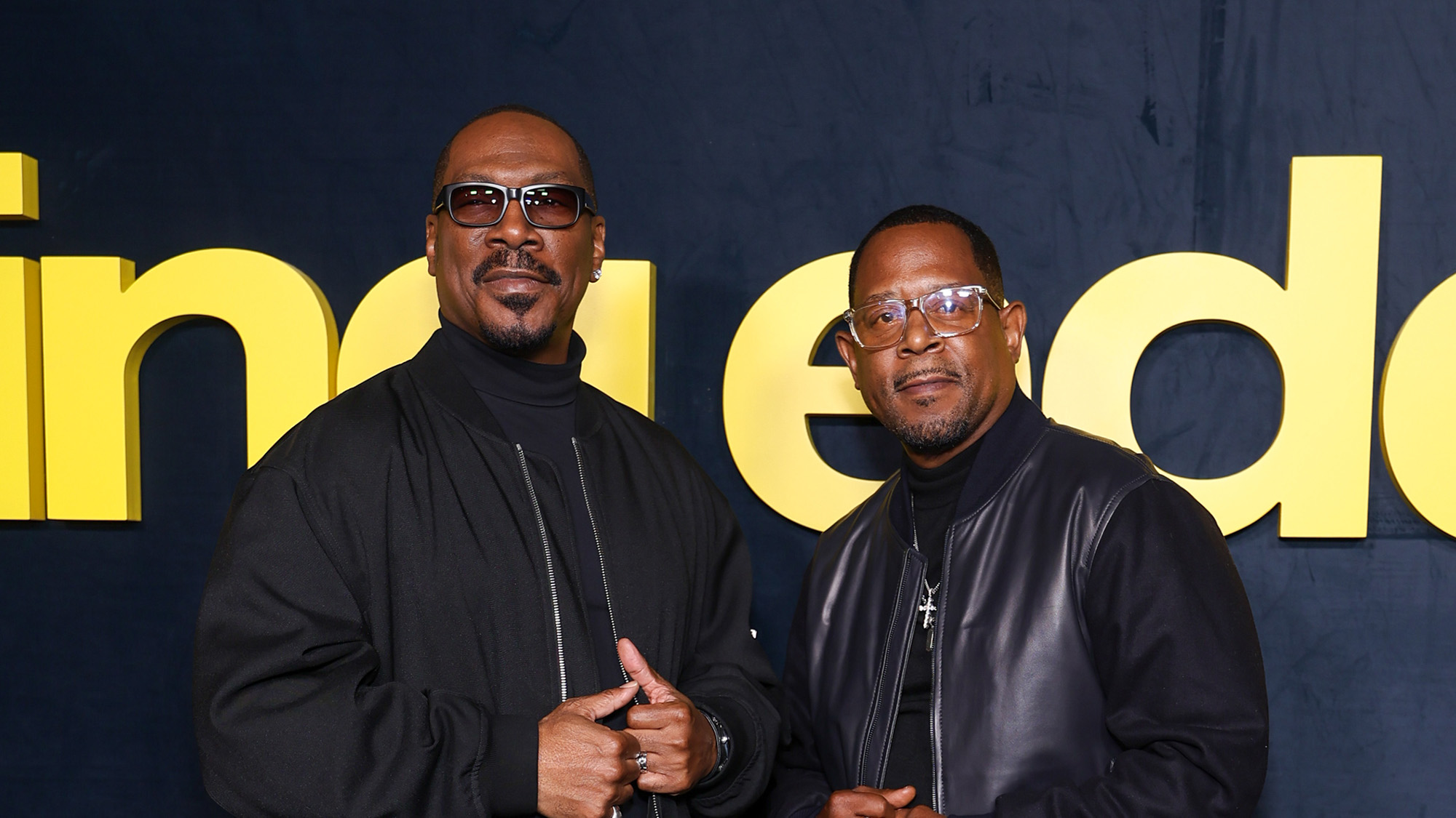 Eddie Murphy and Martin Lawrence both in all black outfits and sunglasses on the red carpet. They are both looking at the cameras.