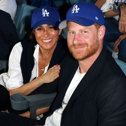 Meghan Markle holding Prince Harry's arm wearing LA Dodgers hats