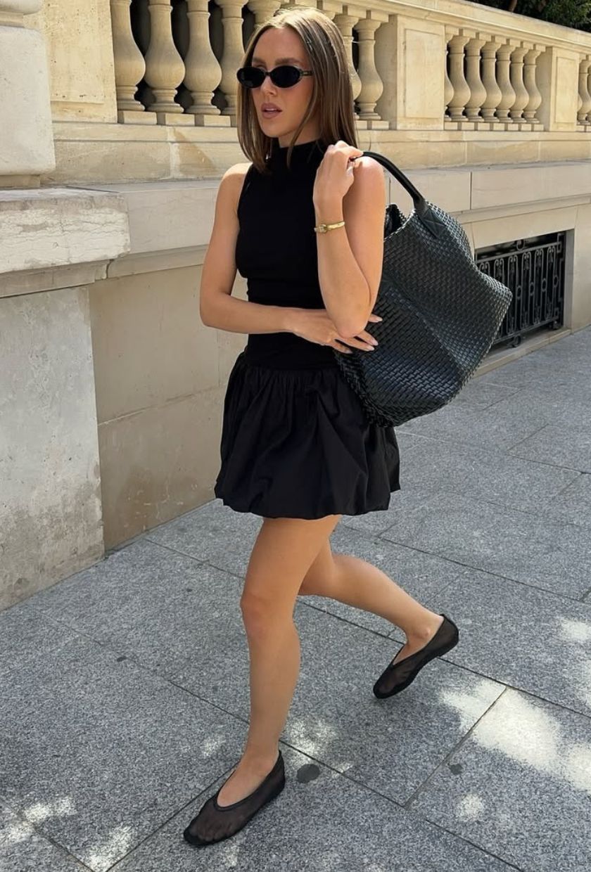 @emmaleger trägt ein schwarzes Minikleid mit Ballonsaum, Ballerinas, Sonnenbrille und Tragetasche