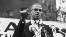 Nation of Islam leader Malcolm X speaking into multiple microphones at a rally, pictured in 1963