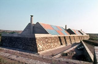 A 1970s photograph of a holiday home by Umberto Riva, made of stone and with a checkered red and blue tiled roof