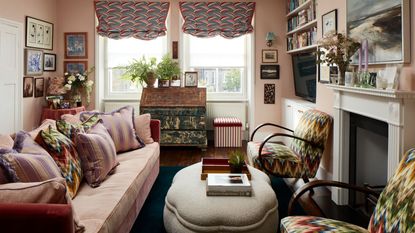 neutral traditional living room with a fireplace, a pink couch with patterned cushions, a boucle ottoman, patterned armchairs and a vintage sideboard