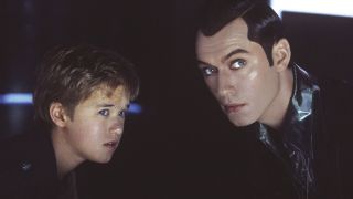 Still from the movie " A.I. Artificial Intelligence." On the left is a young boy (who is actually a robot) and on the right is a man with slick black hair. They're both looking at something in the distance.
