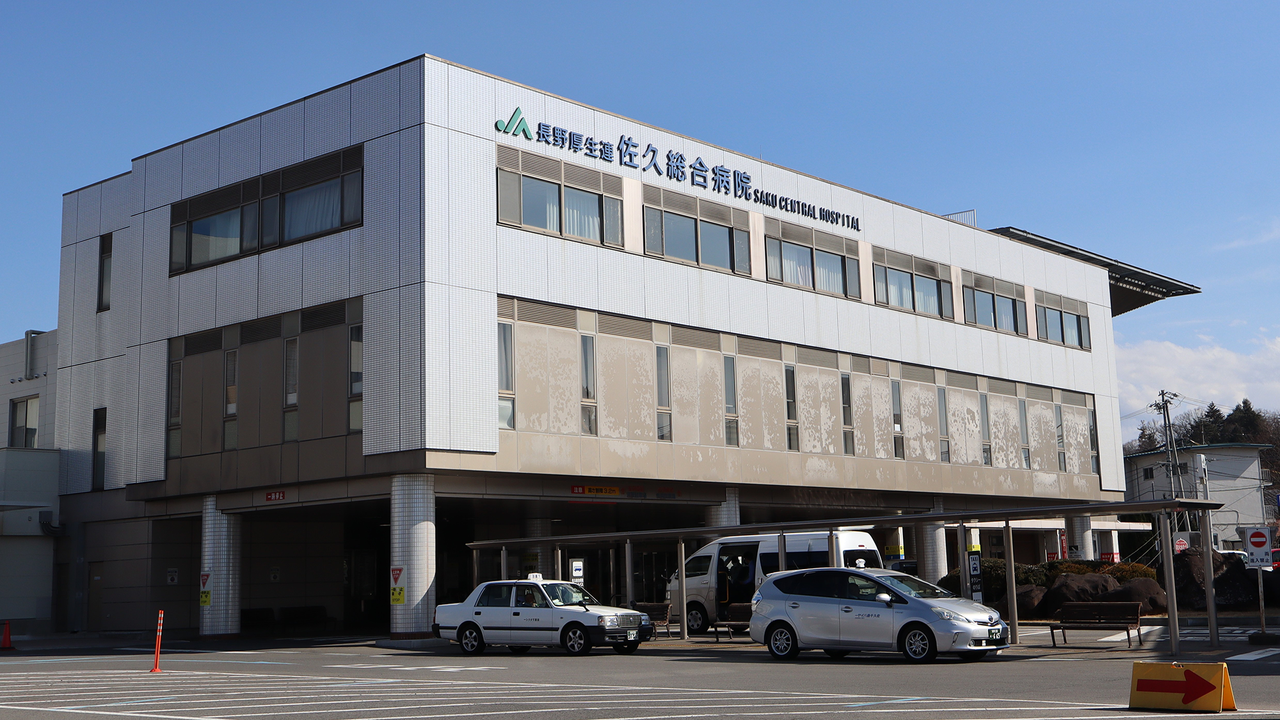 The exterior of Saku Central Hospital, a large building with the hospital's name written on the outside in Japanese and English