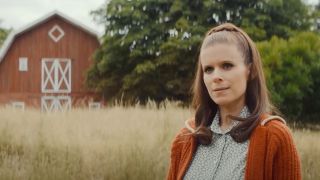 Kate Mara standing in a field near a barn in Black Mirror