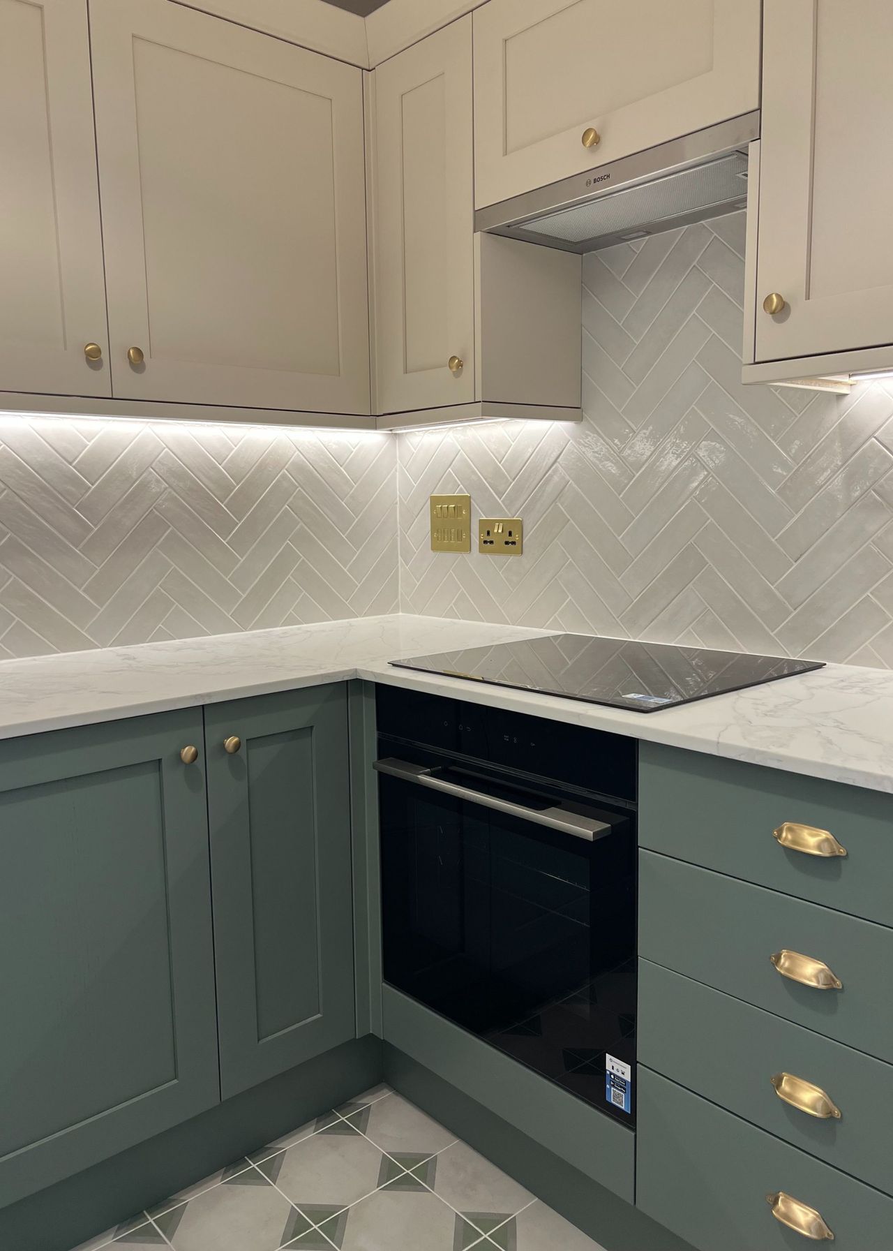 A two tone kitchen with an integrated washing machine, a stove and oven. There is extra storage on the right side with three 4 drawers, a quartz countertop as well as gold handles and features.