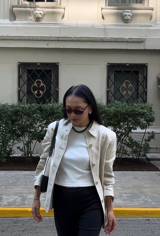 best womens shackets shown on a woman walking wearing a white jacket over a white t-shirt with black trousers, a black shoulder bag, and a green necklace