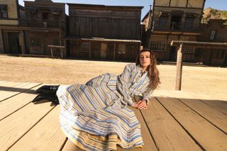 Daisy Edgar-Jones lays in front of Western buildings wearing a blue-and-yellow striped top and skirt from Bottega Veneta.