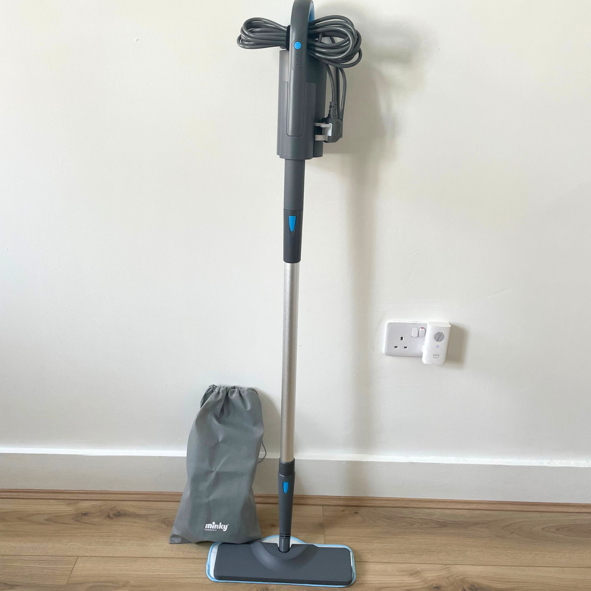 Minky Opti-Clean Steam Cleaner laying against a white wall, with a Minky bag for accessories sitting next to it