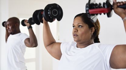 Woman and man exercising with dumbbells at home