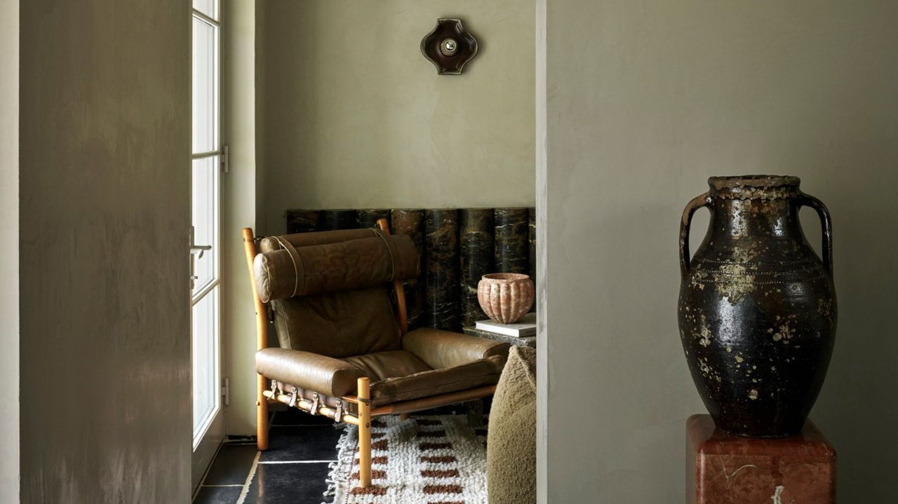 view through living room in moody sage walls with wood and leather chair